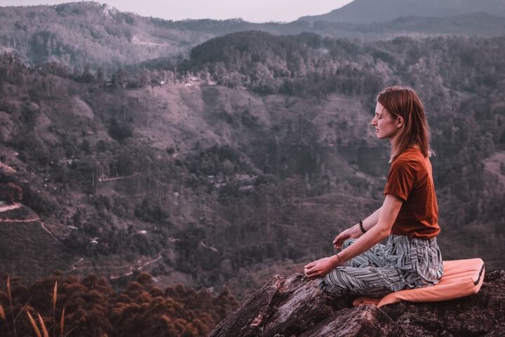 Woman meditating cross-legged on a hillside above a valley