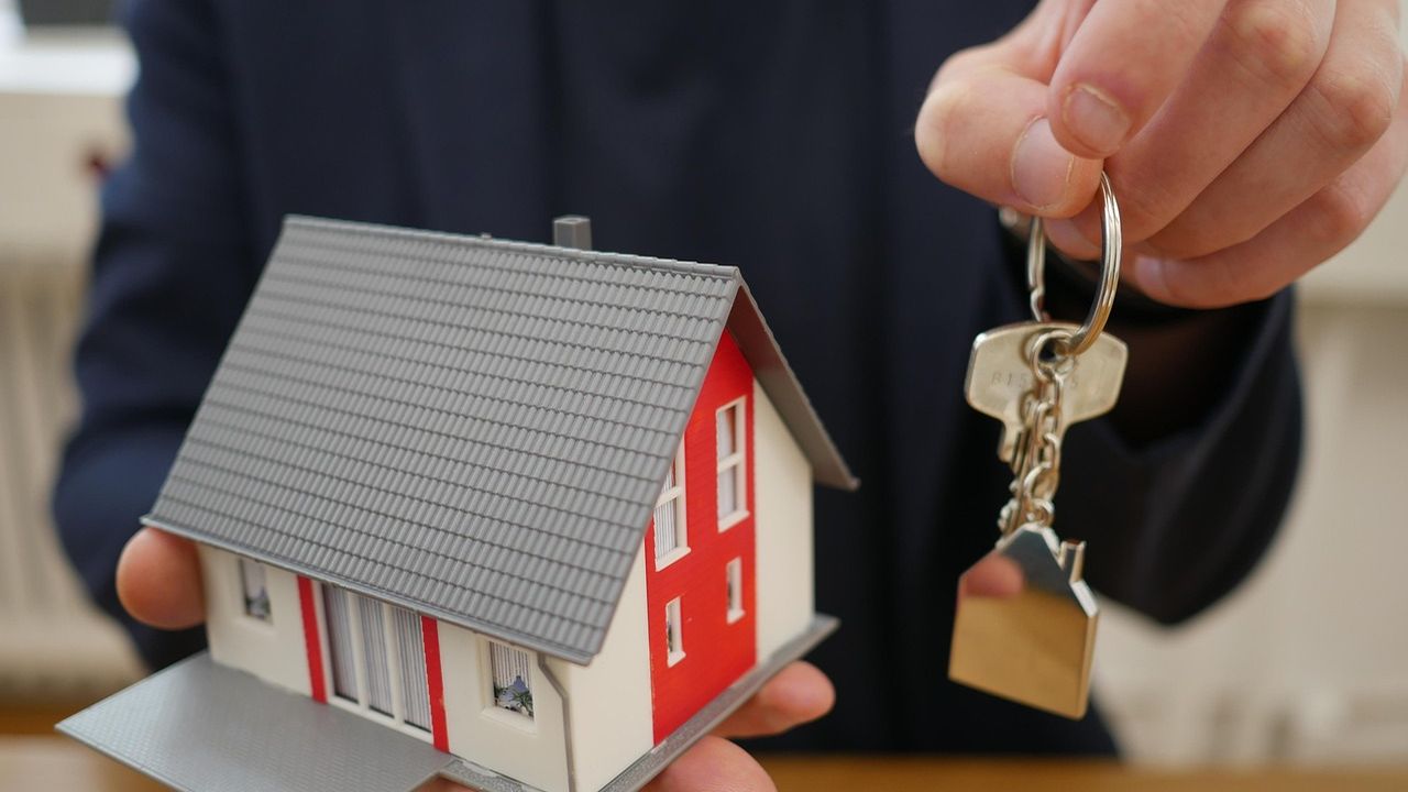 Agent handing over house keys beside a model house