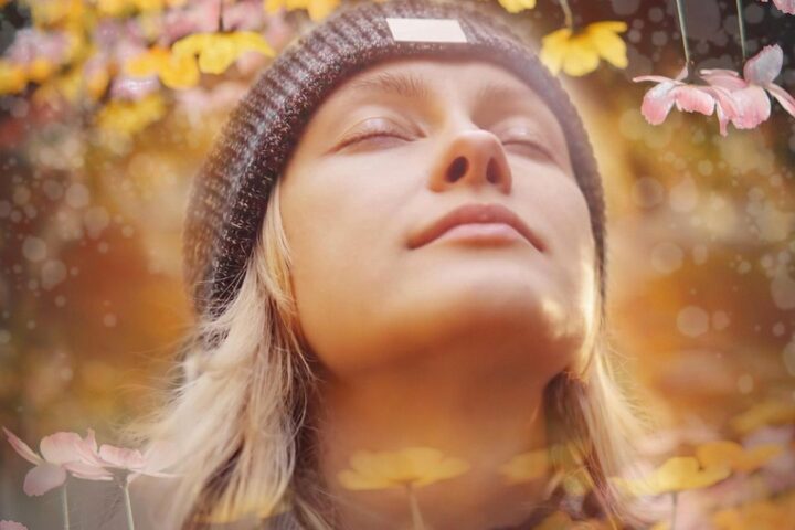 Woman in a woolly hat with eyes closed, smiling in autumn light