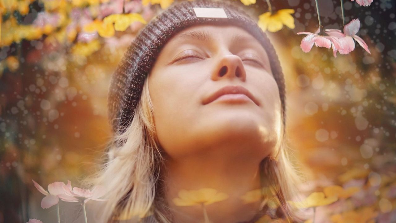 Woman in a woolly hat with eyes closed, smiling in autumn light