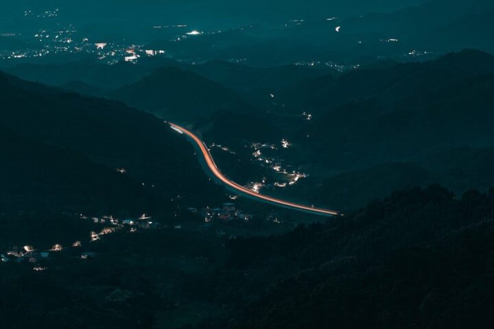 Night landscape, mountains, highway, light trail, landscape at night, nature, hilly area, city lights, road lights, panoramic shot, peaceful night, distant view, quiet landscape, long exposure, mountain silhouette, small town, peaceful atmosphere, rural landscape, night driver, cityscape, quiet evening