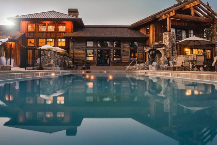 Luxury timber lodge lit up at dusk behind a reflecting pool