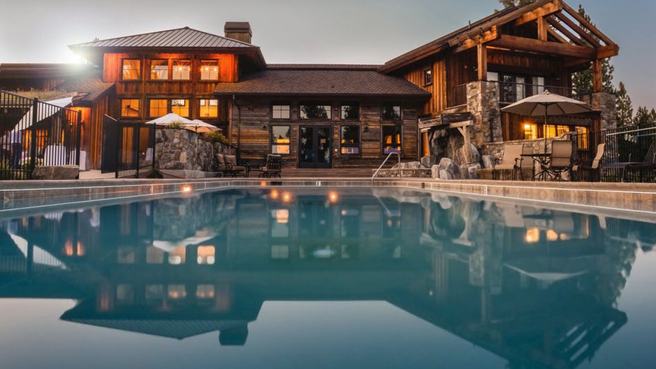 Luxury timber lodge lit up at dusk behind a reflecting pool