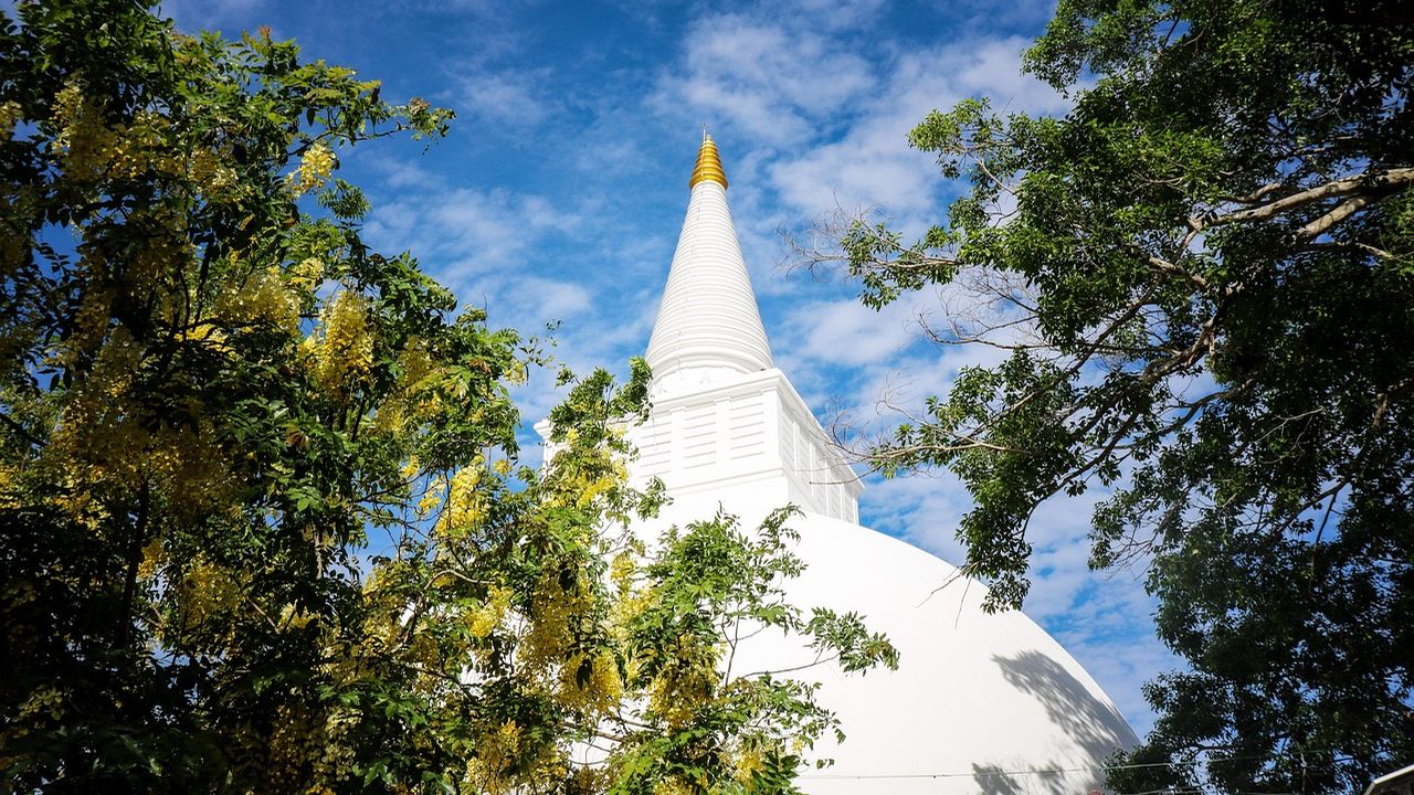 White stupa against a blue sky framed by trees