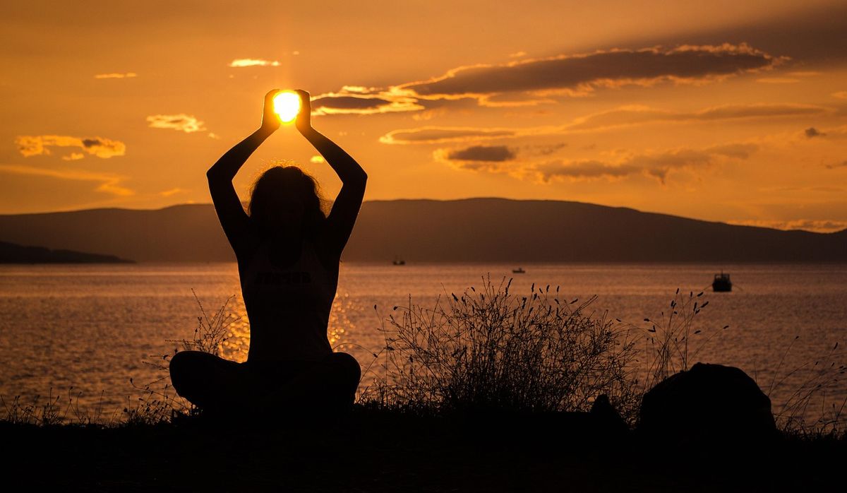 Silhouette of a woman holding up the sun at sunset