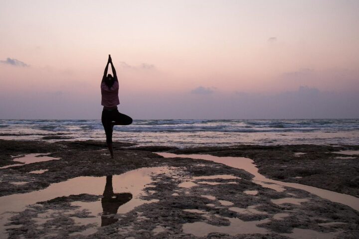 Woman in a yoga tree pose on the shore at dusk