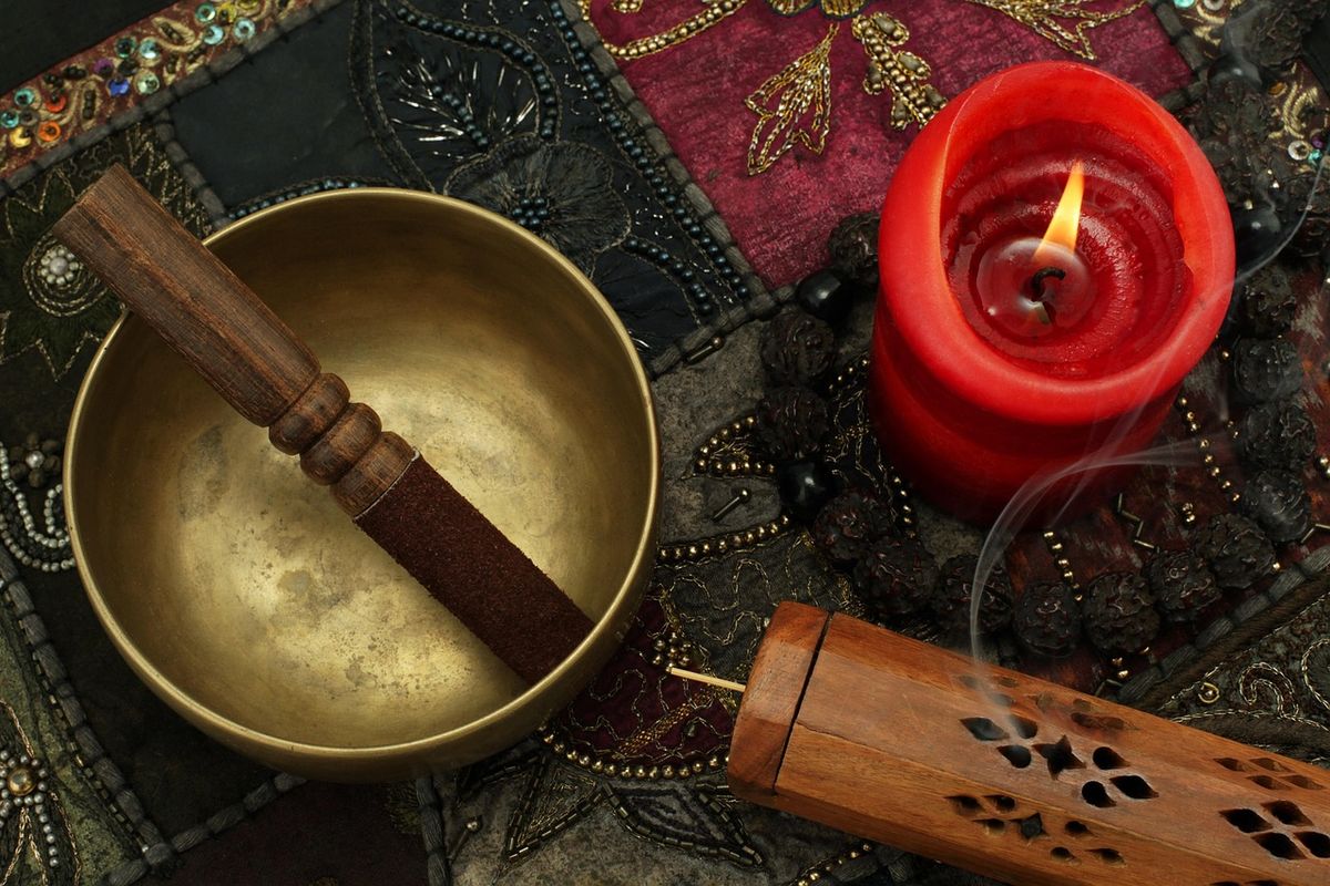 Singing bowl, red candle and incense on a patterned cloth