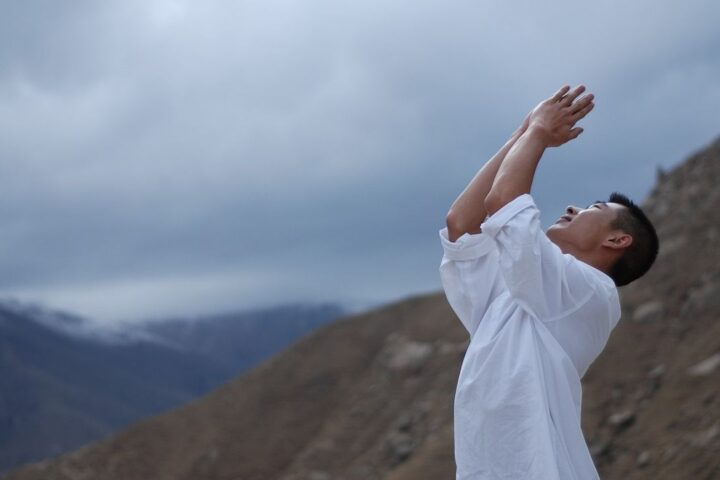 Man in white with arms raised in prayer in the mountains
