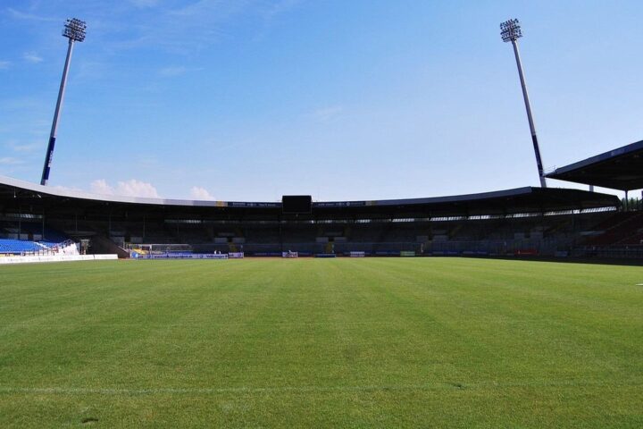 Football stadium with floodlights and green pitch under a blue sky