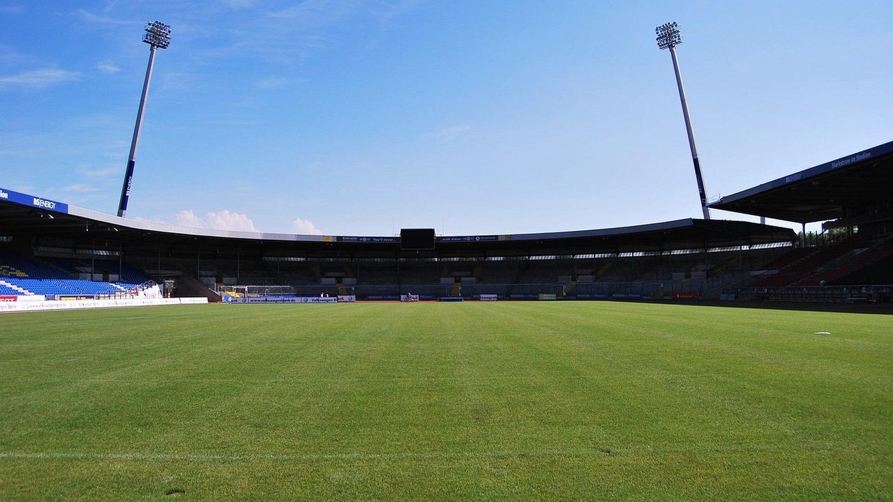 Football stadium with floodlights and green pitch under a blue sky