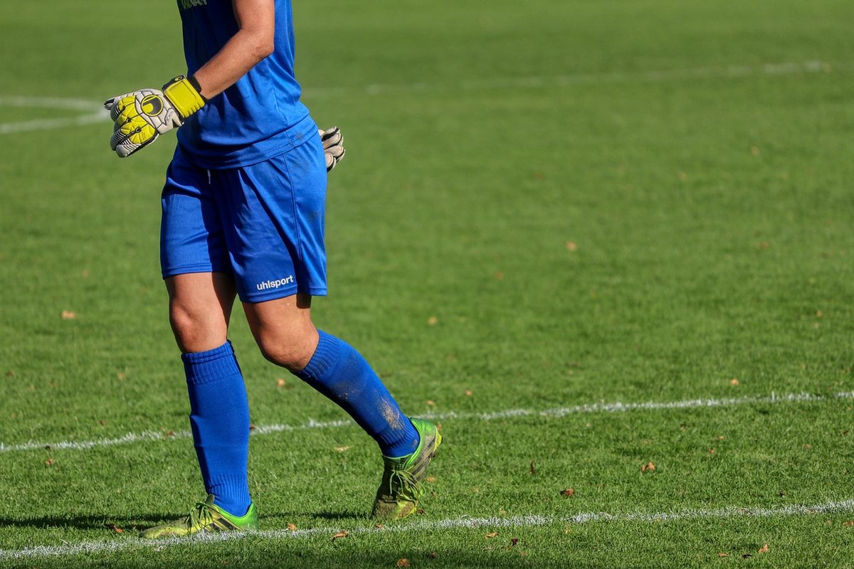 Goalkeeper in blue kit walking across the pitch