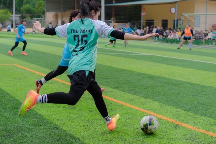 Woman footballer in a teal kit kicking the ball