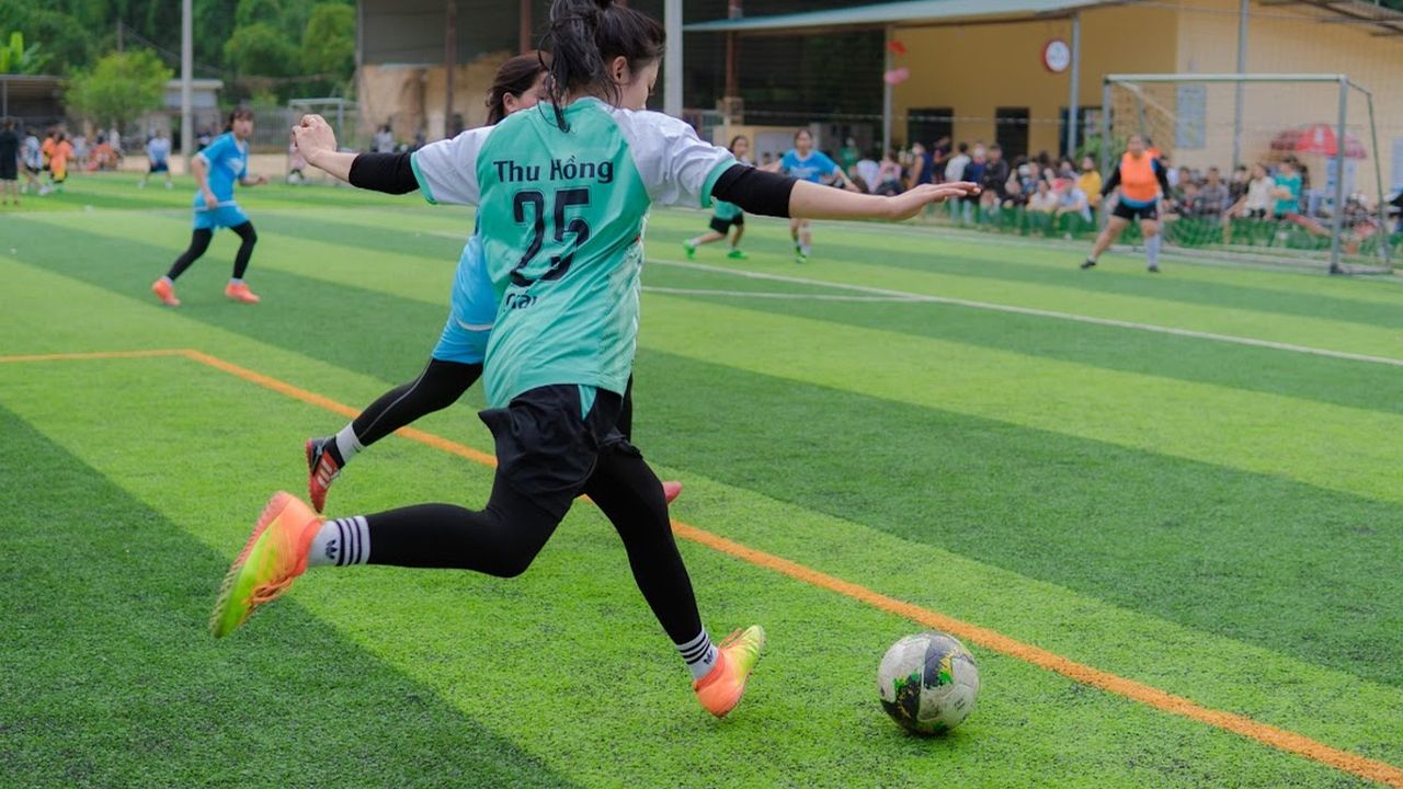 Woman footballer in a teal kit kicking the ball