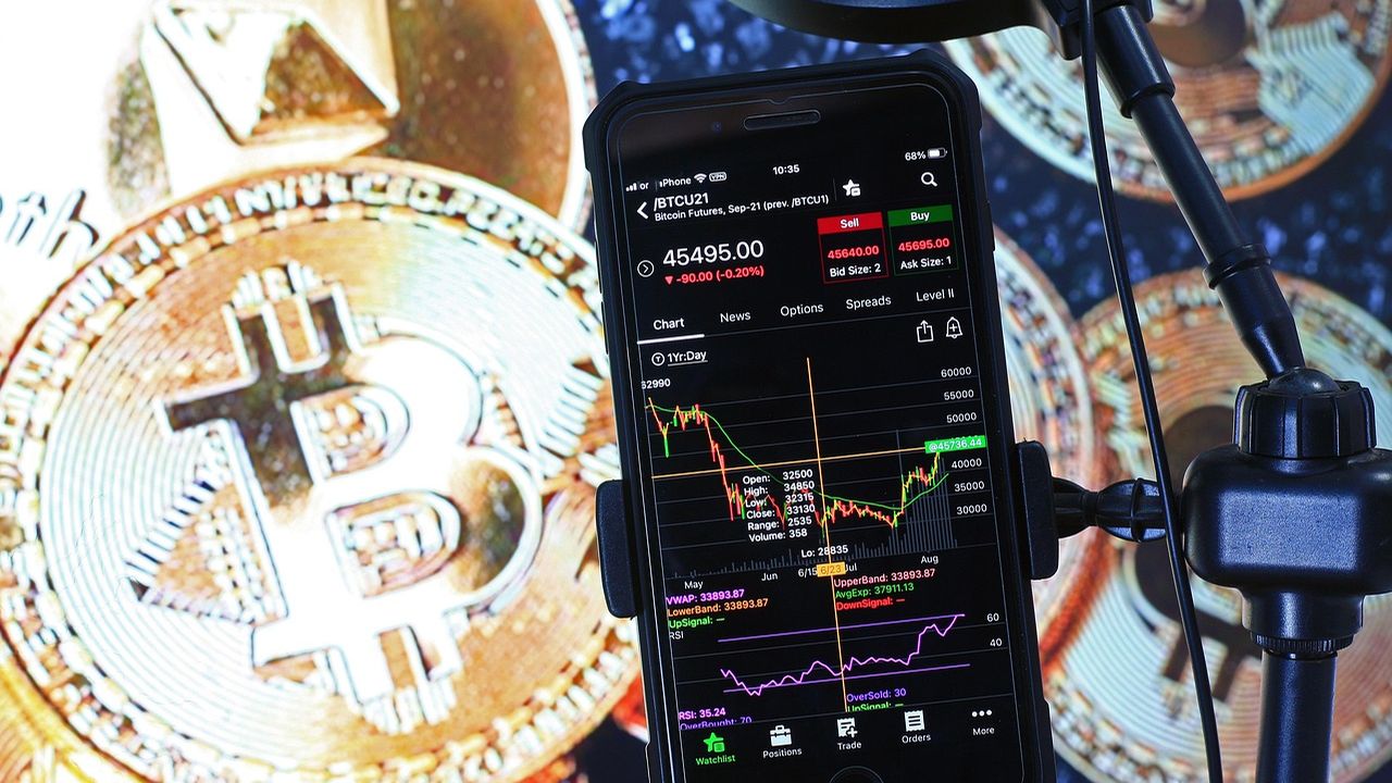 Bitcoin coins beside a phone showing a trading chart