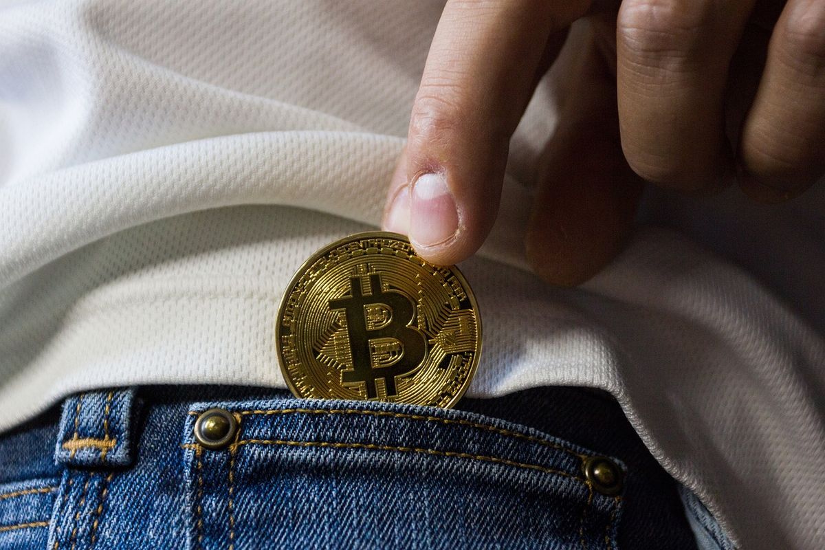 Hand slipping a bitcoin coin into a jeans pocket