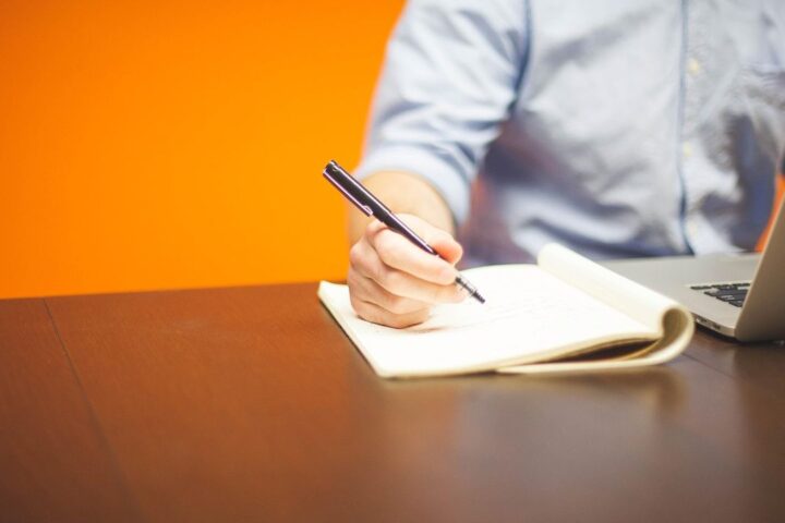 Man writing in a notebook beside a laptop