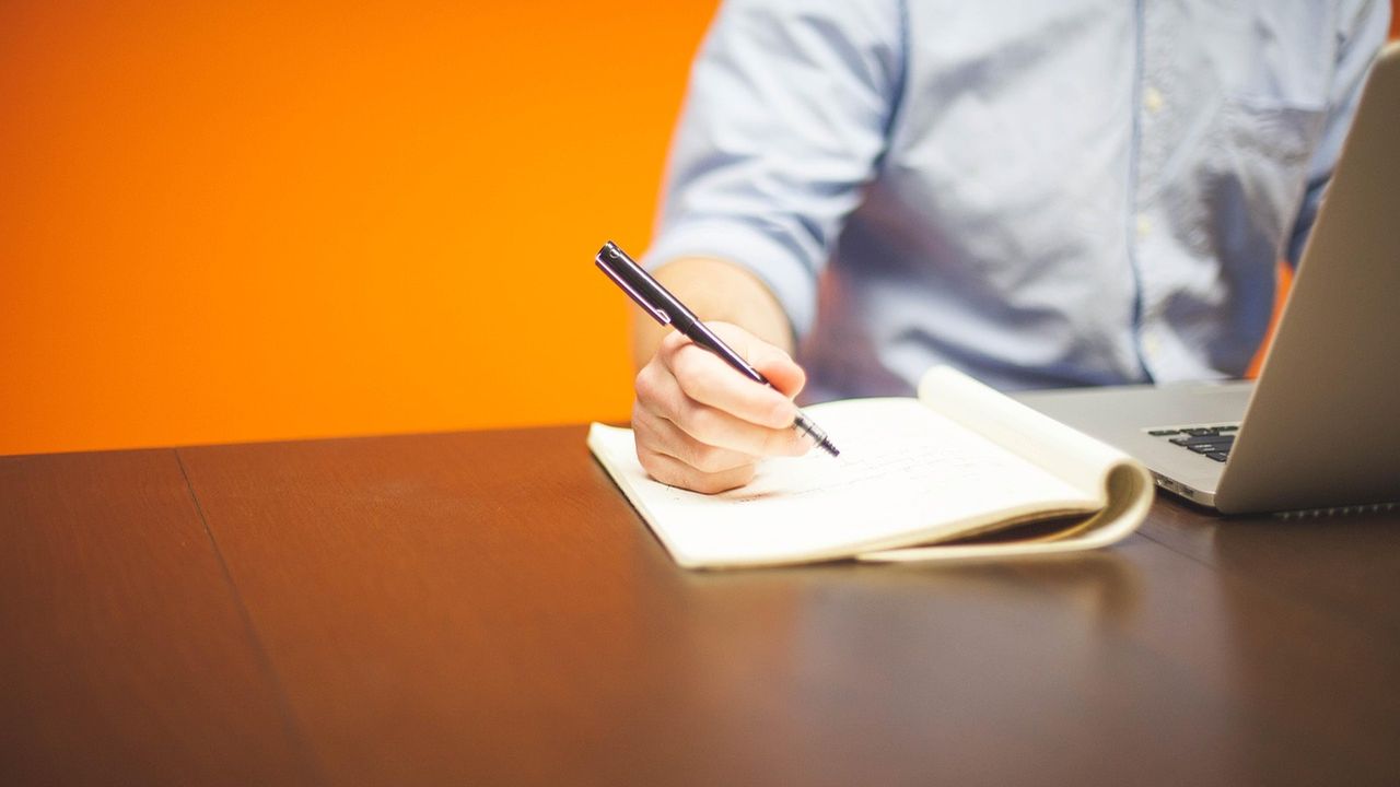 Man writing in a notebook beside a laptop
