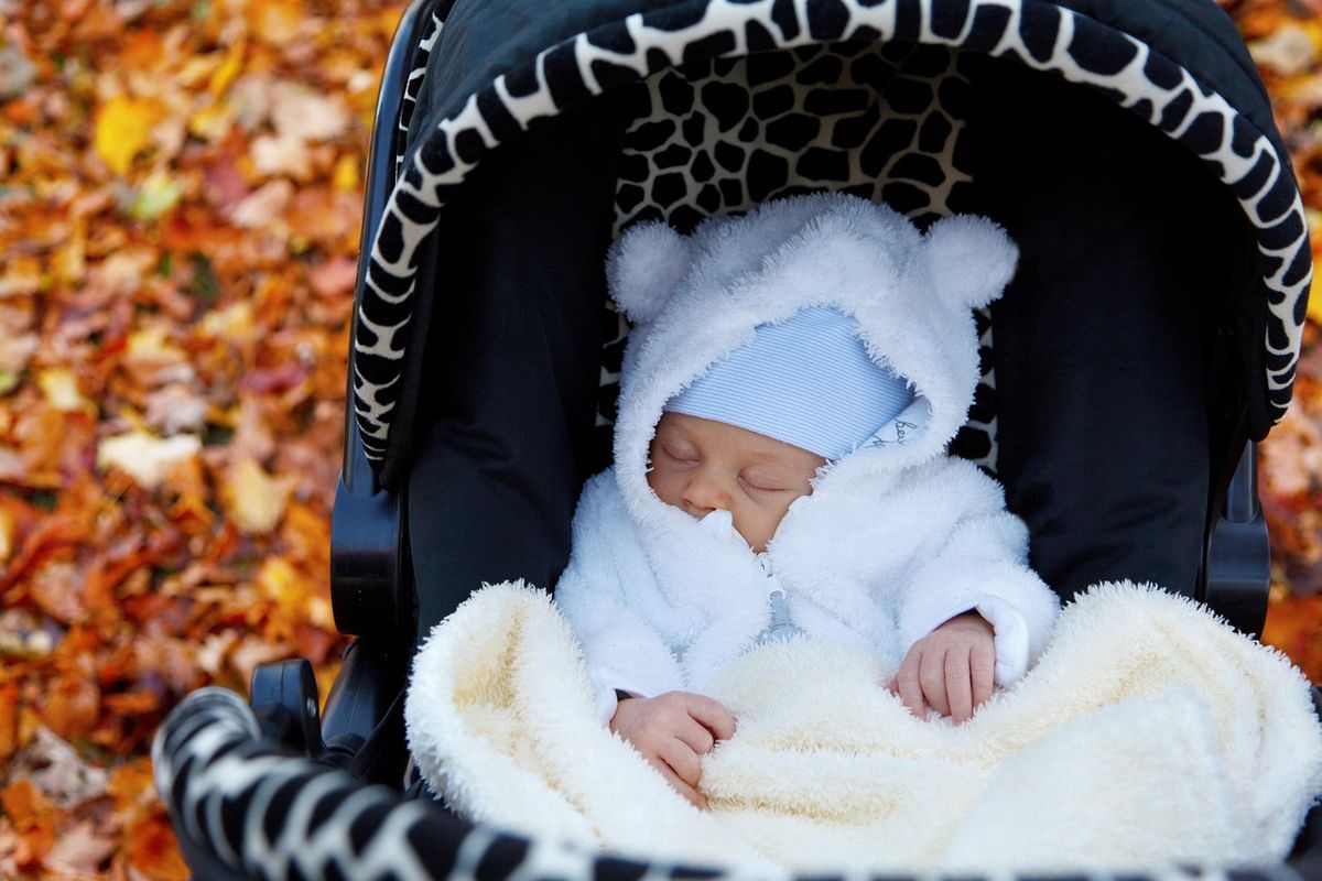 Baby wrapped up warm in a pushchair among autumn leaves