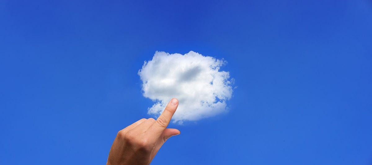 Finger pointing up at a small white cloud in a blue sky