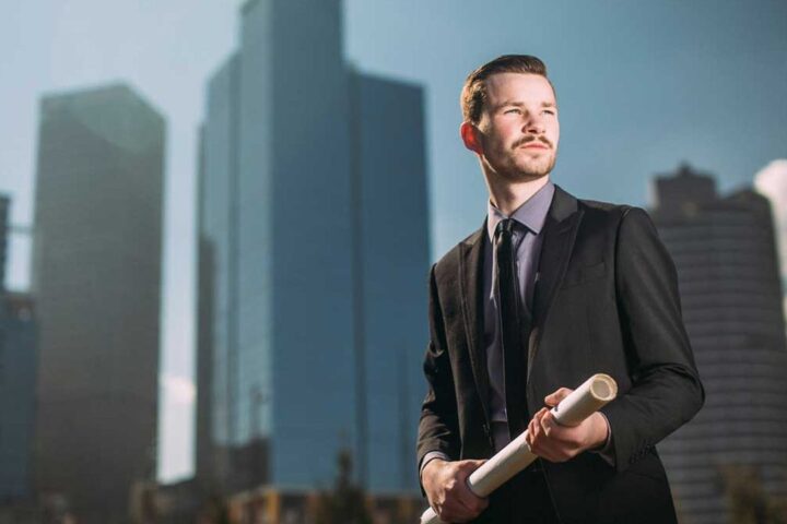 Businessman holding rolled plans in front of skyscrapers