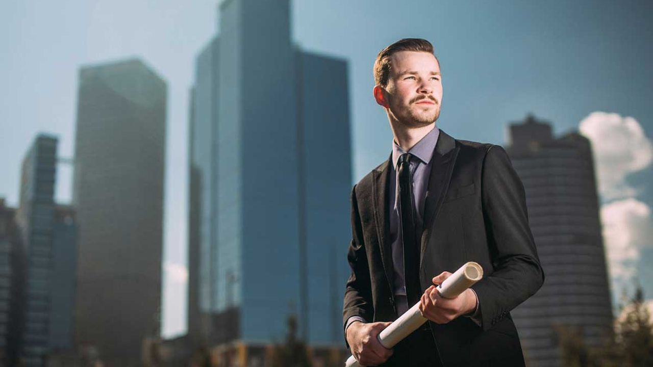 Businessman holding rolled plans in front of skyscrapers