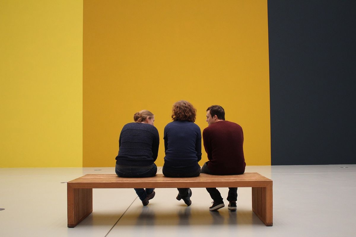 Three people sitting on a bench in front of a yellow gallery wall