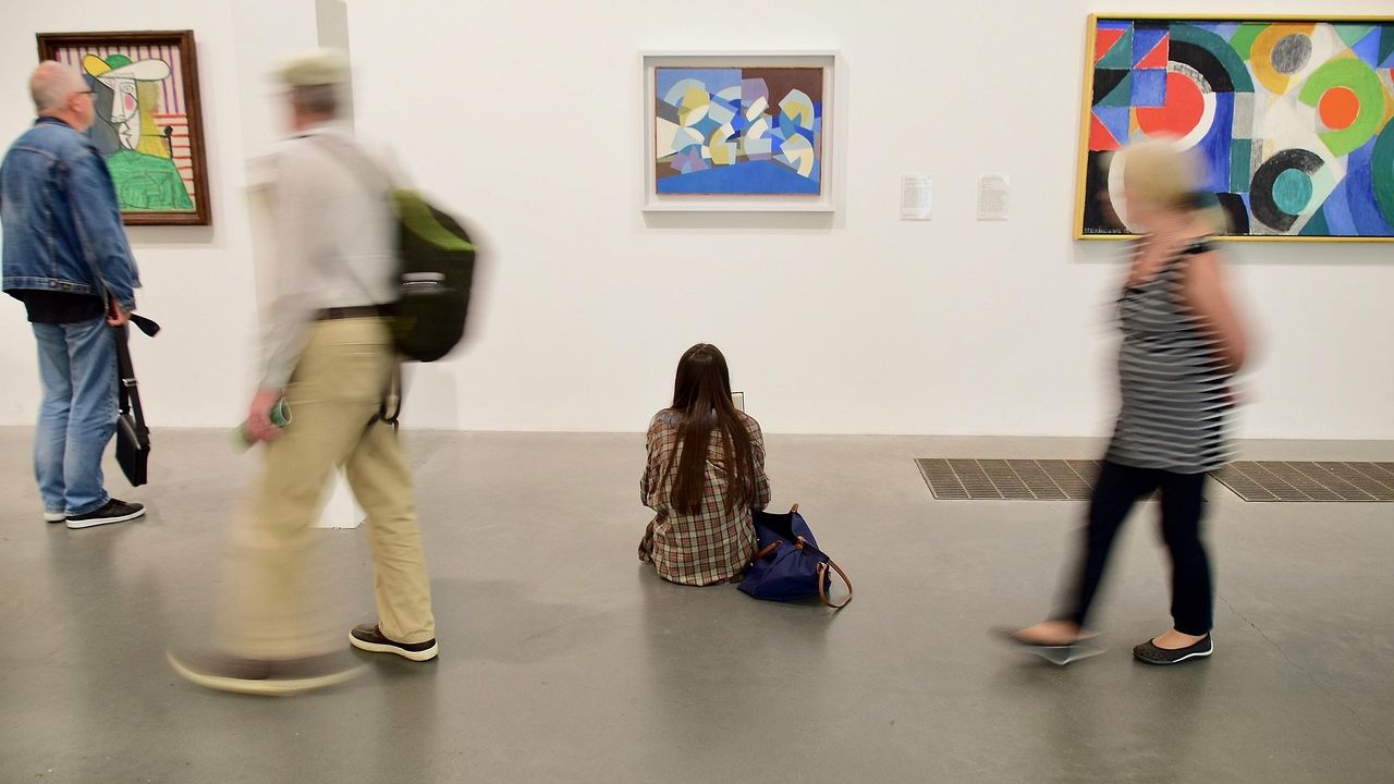 Visitors walking past colourful abstract paintings in a gallery