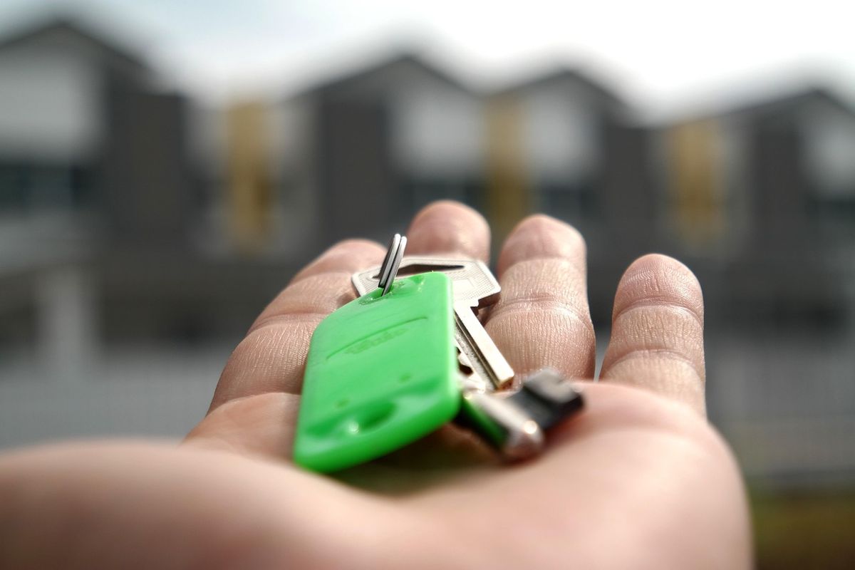 Hand holding house keys with a green key fob