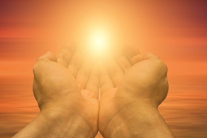 Cupped hands raised towards a glowing sunset